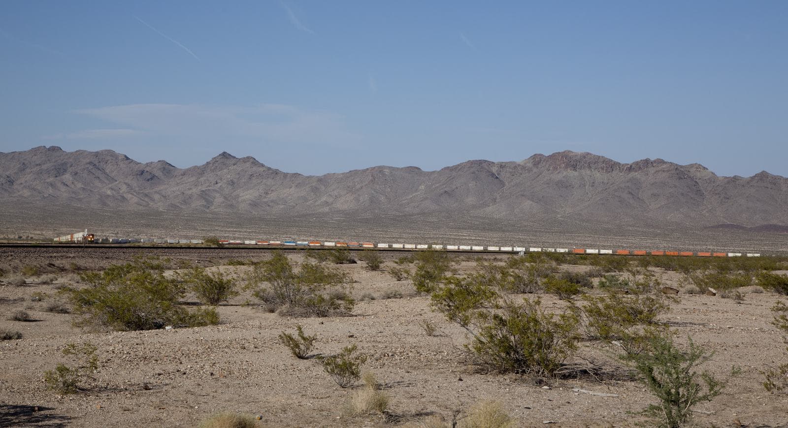 Long freight train crossing a desert plain beneath rugged mountains